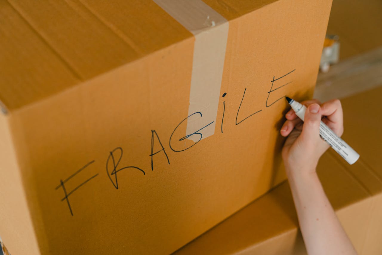 heros-img From above of crop unrecognizable person writing with marker on cardboard box with fragile products before relocation