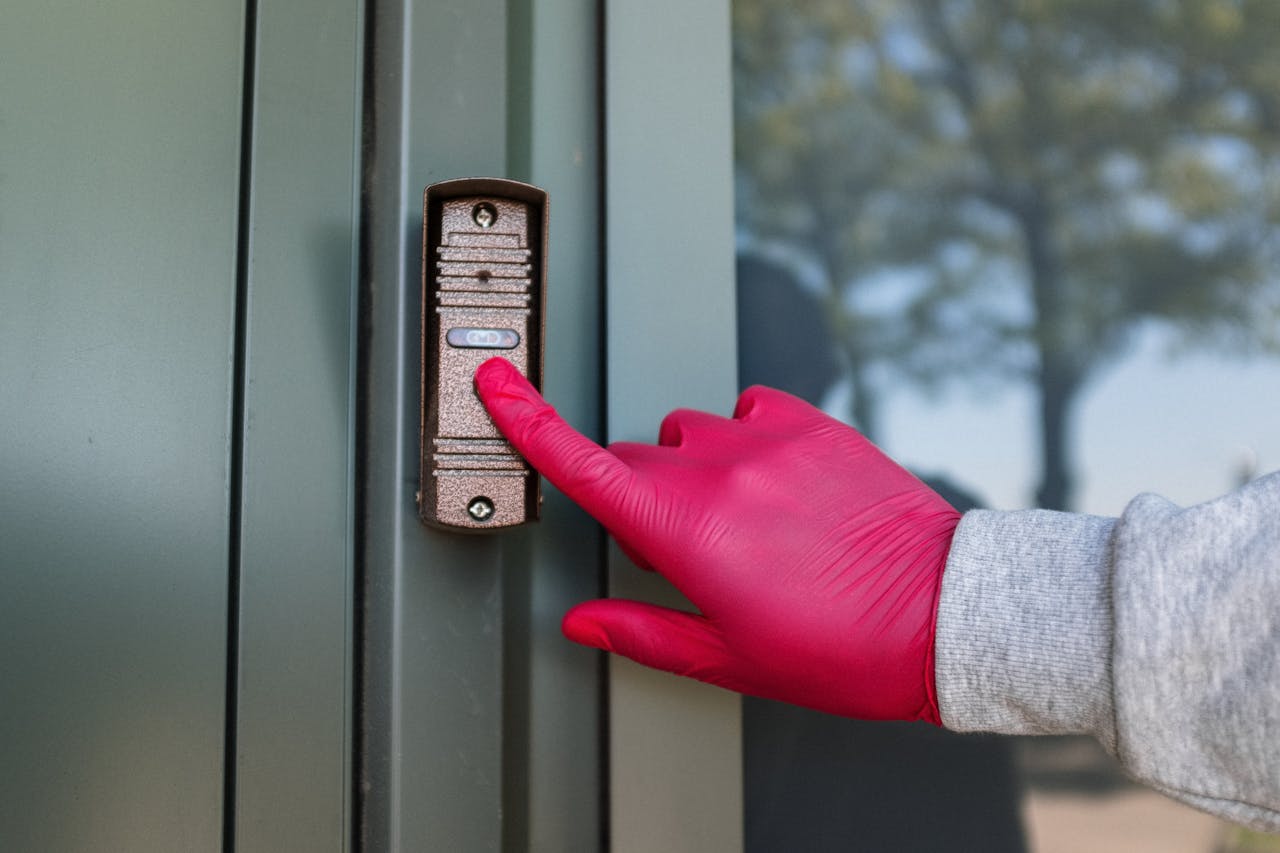 about-us-02 A red gloved hand presses a modern doorbell on a metal door, depicting security and service.