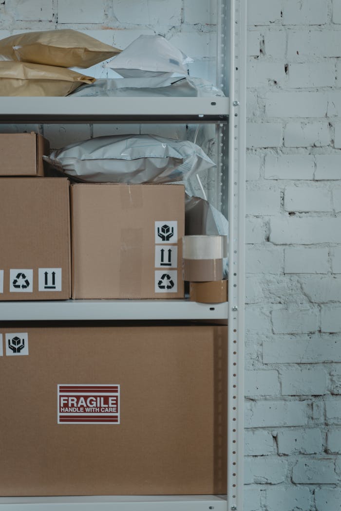 services-01 A warehouse shelf with labeled cardboard boxes and packing materials against a brick wall.