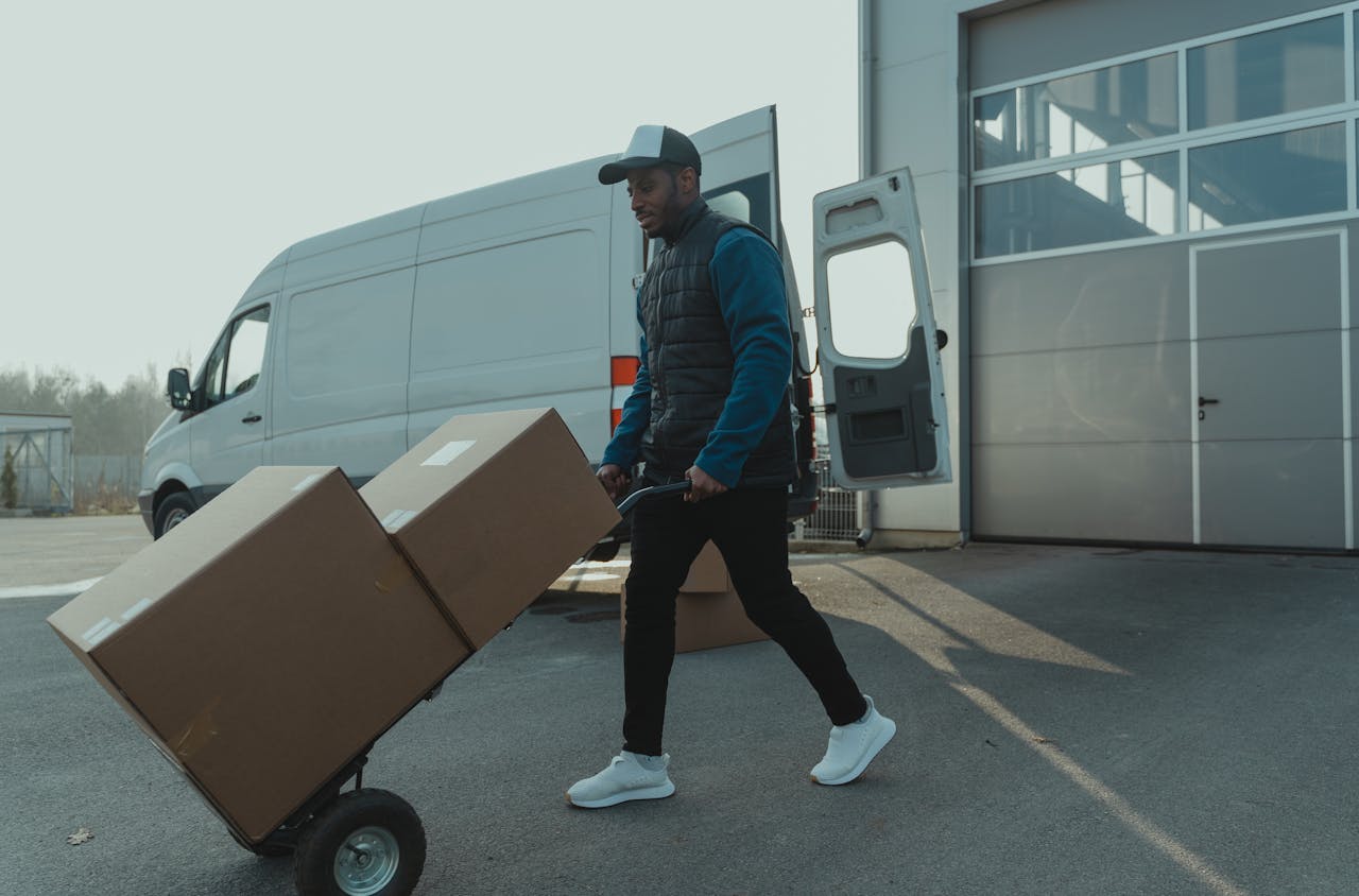 services-04 Courier pushing a trolley with boxes near a van at a warehouse, showcasing delivery services.